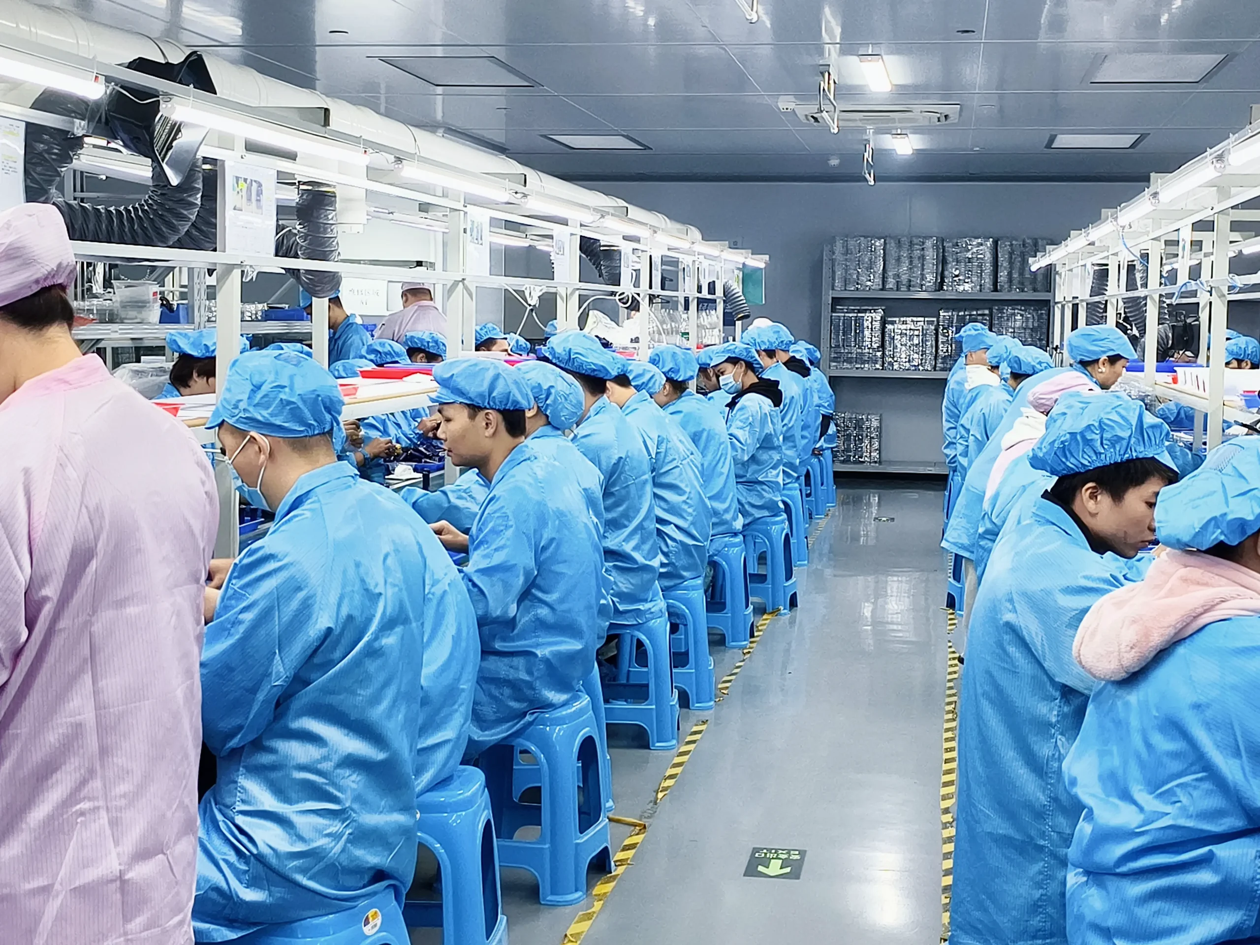 Rows of workers in blue cleanroom uniforms hand-assembling disposable vape components at Vape ODM Factory production floor